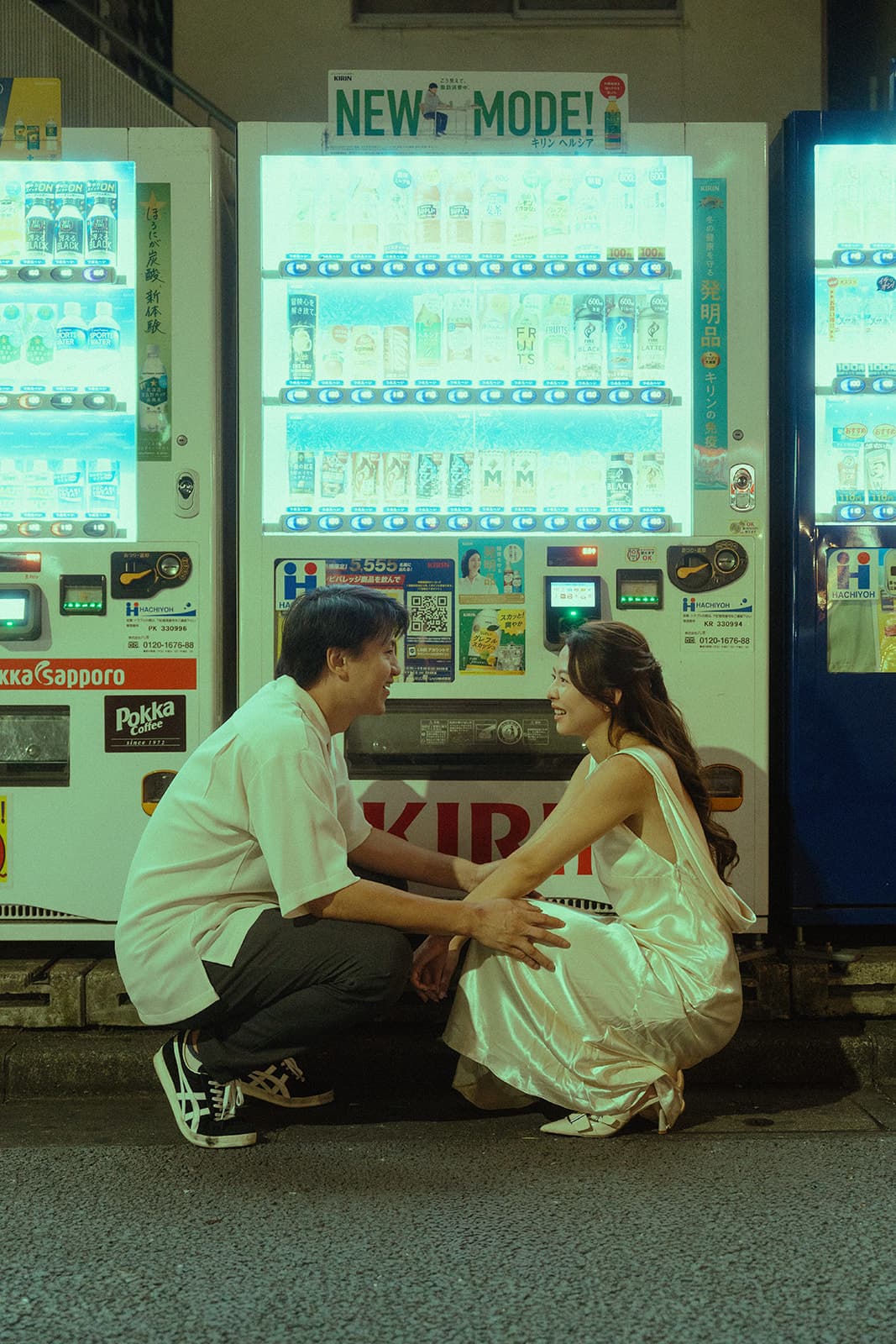 Crouching face to face by glowing vending machines at night